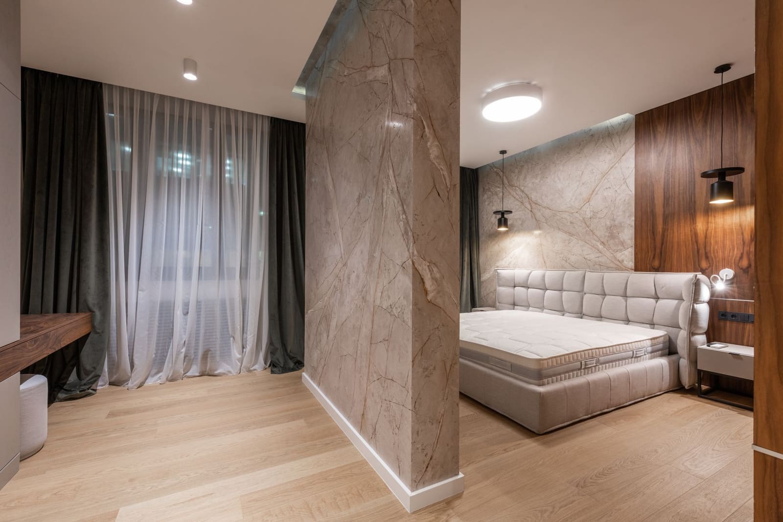 A calm bedroom with a stone feature wall, timber panelling and soft curtains