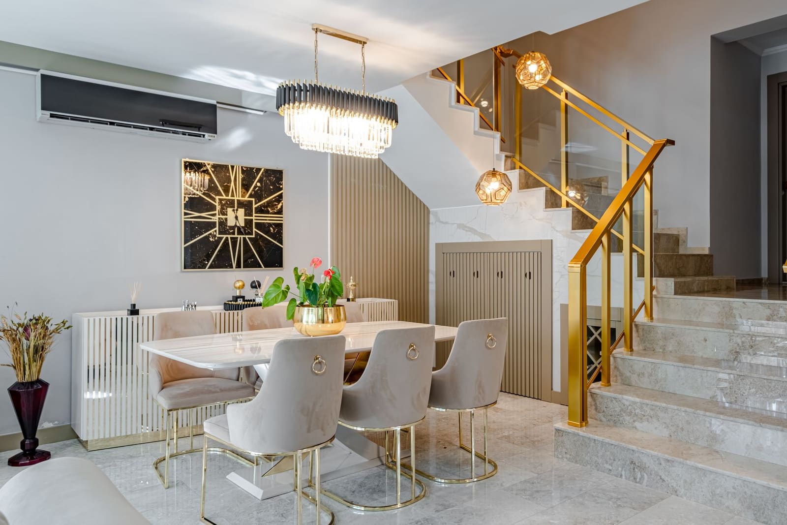 A bright dining area with a crystal chandelier and a gold banister staircase