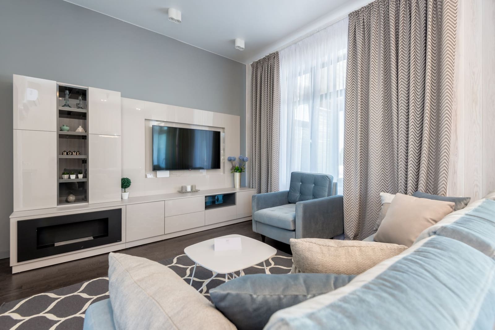 A calm living room with a grey sofa, soft rug and a chandelier